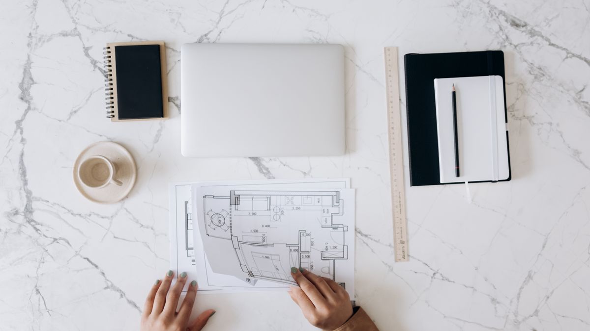 Architekt arbeitet an einem Schreibtisch mit Bauplänen, Notizbuch und Laptop