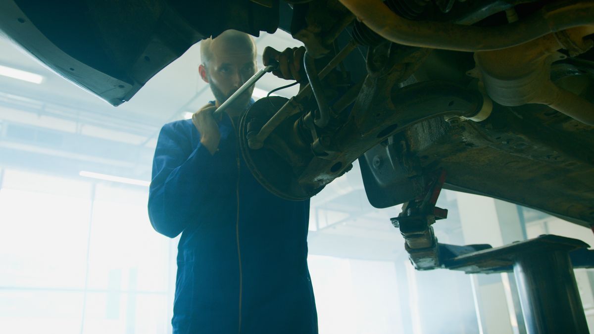 Kfz-Mechaniker hält Werkzeug in der Hand und begutachtet ein Fahrzeug in der Werkstatt