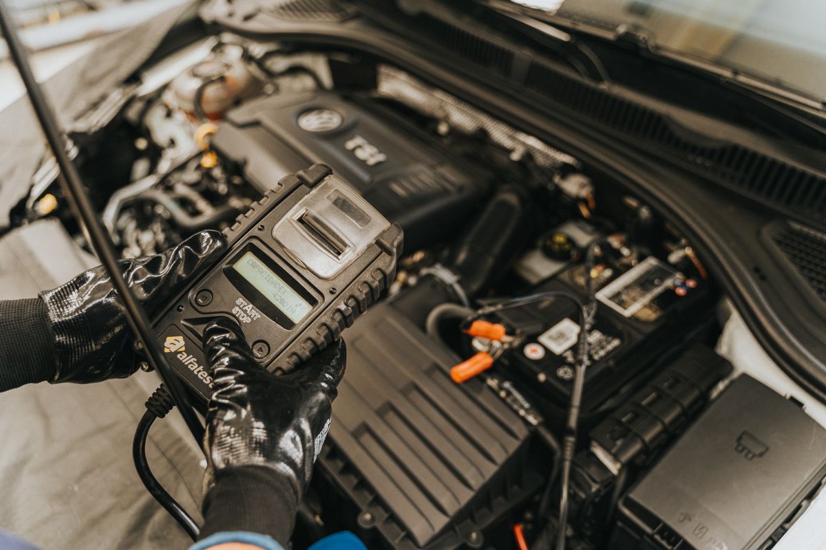 Kfz-Mechaniker führt eine Motordiagnose an einem geöffneten Fahrzeugmotor durch
