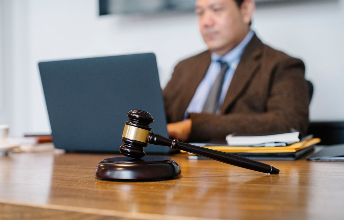 Richterhammer auf Schreibtisch mit Anwalt, der im Hintergrund am Laptop arbeitet